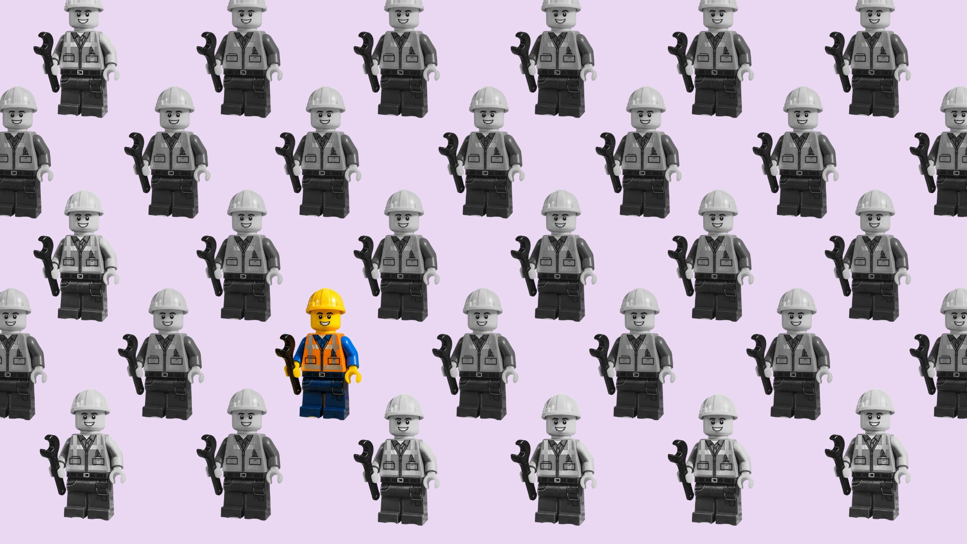 A grid of identical grey Lego construction worker figurines, with a single colourful yellow-and-orange Lego worker standing out in the centre of the crowd. Image of a hard hat hanging on a hat stand.